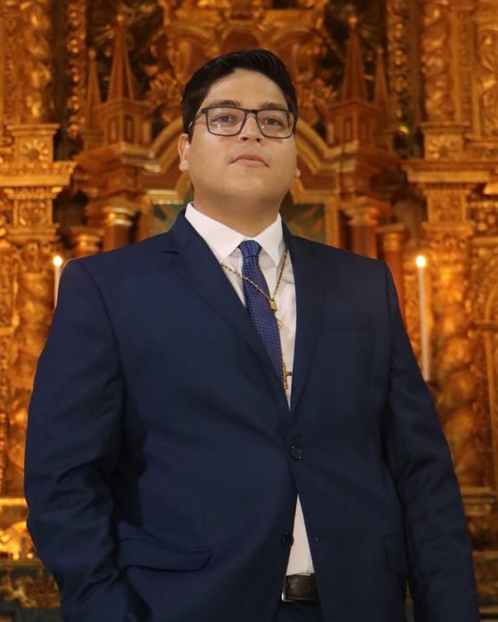 Jório Serra Maia Júnior, comentarista, de terno azul, diante de um retábulo dourado.
